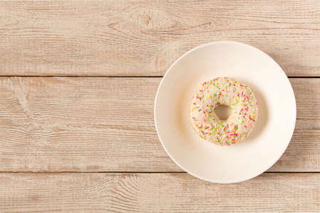 Fresh glazed donut with colorful sprinkles on a white plateの写真素材