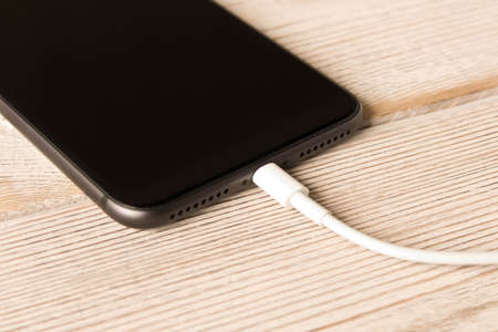 Smartphone on charge. On the  wooden table. Close up