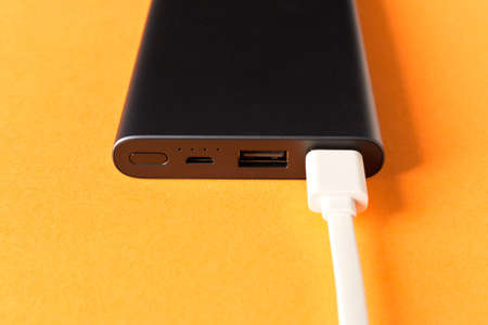 Black power Bank with adapter for charging mobile devices on orange backgroundの写真素材