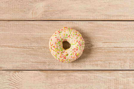 Fresh glazed donut with colorful sprinkles on a wooden tableの写真素材