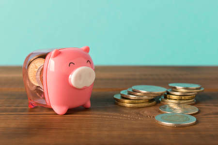 Little piggy Bank and a few coins on the wooden table. Close up. The concept of saving money