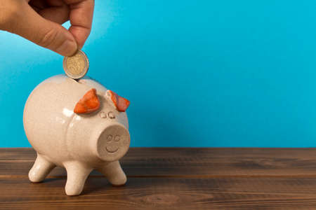 A man's hand putting a coin in a piggy Bank. The concept of saving moneyの写真素材