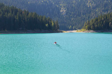 A small boat with people in the middle of a beautiful lake. On the background of picturesque nature.