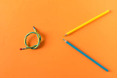 Colored pencils with one flexible pencil on orange background. The concept of flexibility in...