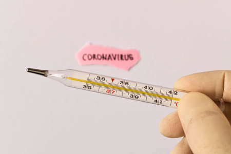 Coronavirus. 2019-nCoV. A human hand with a thermometer and the inscription CORONAVIRUS on a piece of paper on a light background. The concept of virus protection. Selective focus.の写真素材