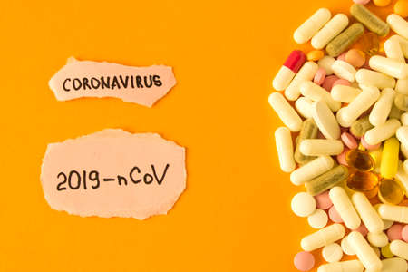 Coronavirus. 2019-nCoV. Scattered pills and the inscription coronavirus on a piece of paper on an orange background. The concept of virus protection. Selective focus.の写真素材