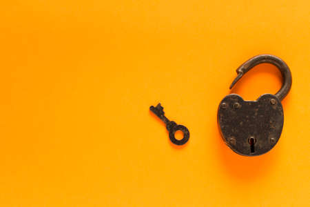 Old padlock with key on a orange background. Security concept. Selective focus