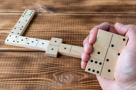 Domino. A human hand with a Domino. A game of dominoes on a wooden tableの写真素材