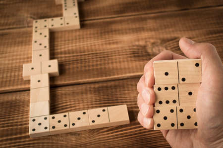Domino. A human hand with a Domino. A game of dominoes on a wooden tableの写真素材