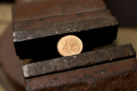 Coin 2 Euro cents in a metal vise. Concept of economic problems. Selective focus. Close up