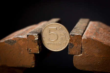 A 5-ruble coin in a metal vise. Concept of economic problems. Selective focus. Close up