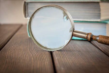 An old magnifying glass and a stack of books on a wooden table. The concept of getting knowledge from books. Selective focusの写真素材