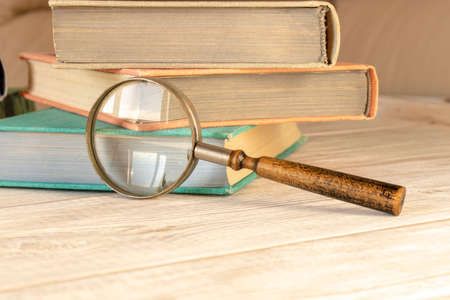 An old magnifying glass and a stack of books on a wooden table. The concept of getting knowledge from books. Selective focusの写真素材