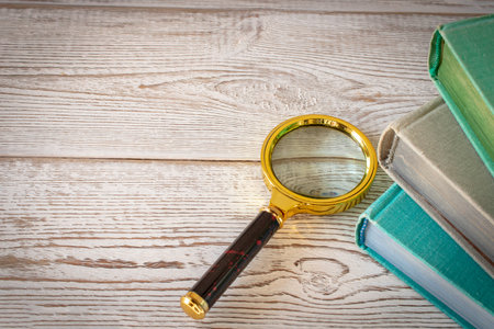 A magnifying glass and a stack of books on a wooden table. The concept of getting knowledge from books. Selective focusの写真素材