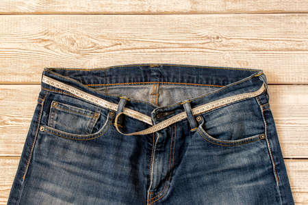 Measuring tape for weight loss in jeans on a wooden background. The concept of being overweight. Selective focusの写真素材