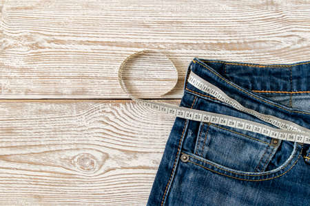 Measuring tape for weight loss in jeans on a wooden background. The concept of being overweight....