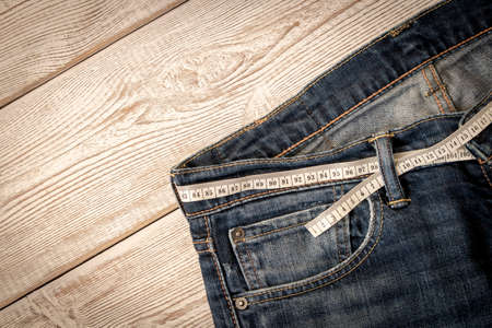 Measuring tape for weight loss in jeans on a wooden background. The concept of being overweight. Selective focusの写真素材