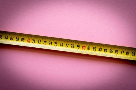 Yellow measuring tape on a pink background. Close-up