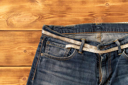 Measuring tape for weight loss in jeans on a wooden background. The concept of being overweight....
