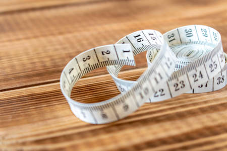 White measuring tape on a wooden background. Close-up