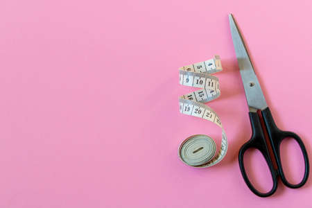 White measuring tape and scissors on a pink background. Close-upの写真素材