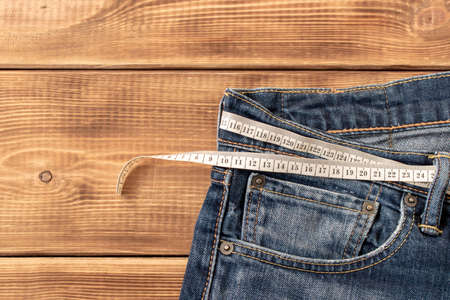 Measuring tape for weight loss in jeans on a wooden background. The concept of being overweight. Selective focusの写真素材