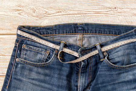 Measuring tape for weight loss in jeans on a wooden background. The concept of being overweight. Selective focusの写真素材
