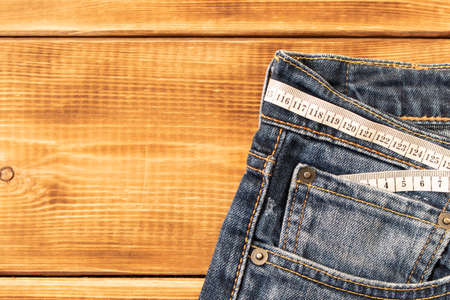 Measuring tape for weight loss in jeans on a wooden background. The concept of being overweight. Selective focusの写真素材