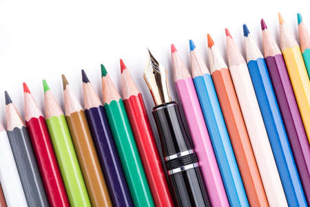 Colored pencils with fountain pen in the middle over whiteの写真素材
