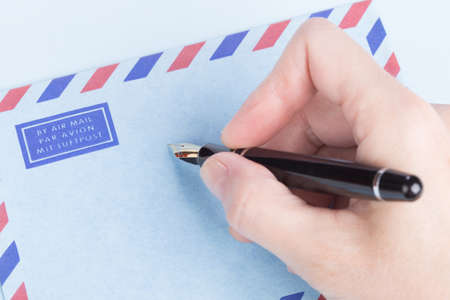 female hand signs airmail envelope on blue paper for lettersの写真素材