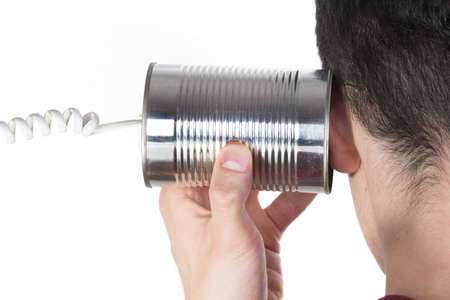 Male hand holding a tin can phone to his ear over whiteの写真素材