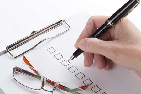 Female hand fills a document attached to the clipboard over whiteの写真素材