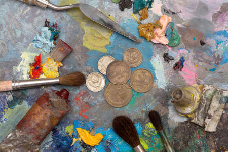 Paint brushes and old coins over old wooden palletの写真素材