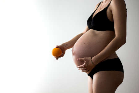 pregnant woman in lingerie comparing her belly to an orangeの写真素材