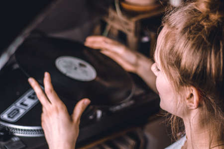 young woman putting on a vinyl record at homeの写真素材