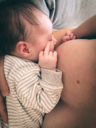 cute newborn baby showing middle finger while drinking milk from mother's breastの写真素材