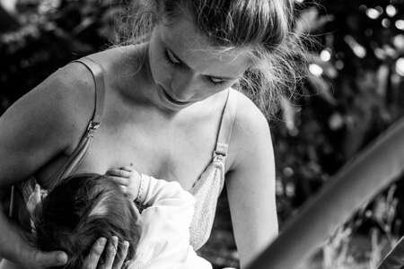 portrait of a beautiful young mother breastfeeding her newborn baby in the gardenの写真素材