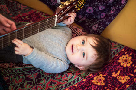 Baby is making music with a guitar at home