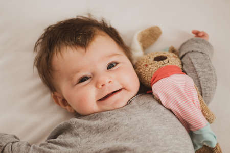 happy baby with bunny soft toy lying in bed
