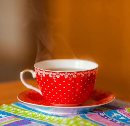 Hot tea in a red Cup with a watch over on the color napkinの写真素材