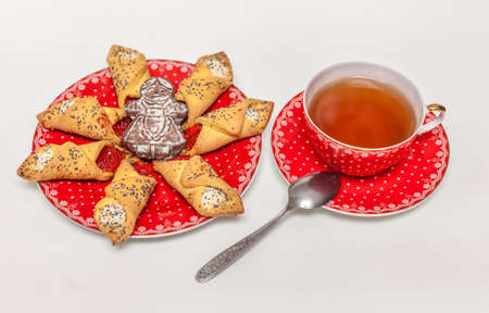 Red Cup with black tea, red plate of cookies with a red jam and poppy seeds and ginger cookies in the shape of little men on a white backgroundの写真素材