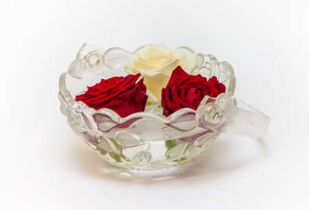One white and two red roses in a glass vase on a white backgroundの写真素材