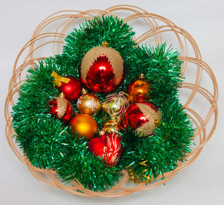 Red and gold Christmas balls with green tinsel on a plate made of wickerの写真素材