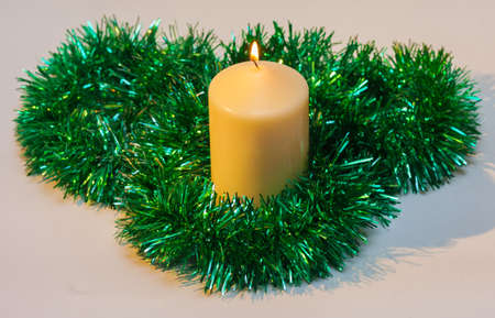 Burning Christmas candle with green tinselの写真素材