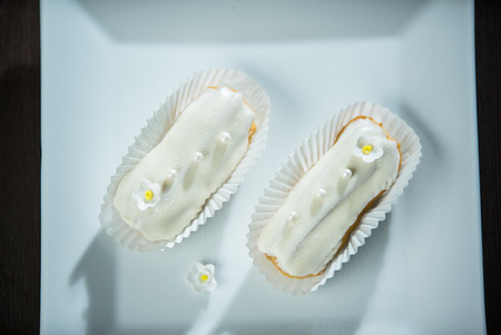 Tasty eclairs with white chocolate glaze and pearls on top of a white plate