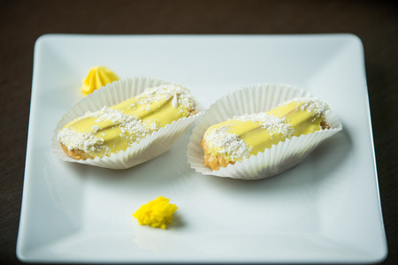 Delicious dessert. Yellow eclair with coconut chips on a white plate