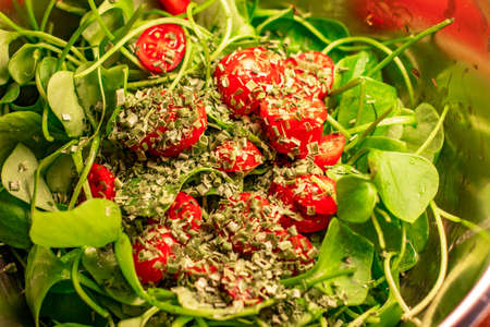 salad made from small tomatoes, cherry tomatoes, green broad leaves and thin stalks with small cut dry herbs in a metal bowlの写真素材