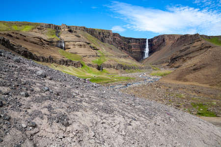 A severe waterfall in the mountains among the rocks. High quality photo. Stone valley and mountain range at horizon under blue sky.の写真素材