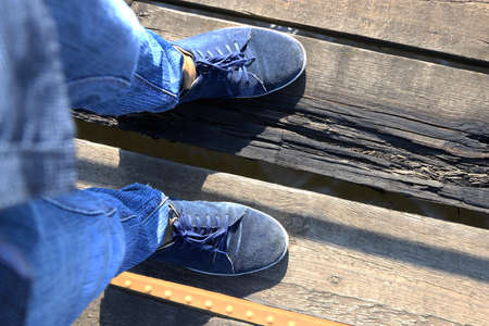 The feet of a man stand on an unstable wooden bridge.