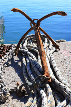 An old cruciform anchor lies on the shore with ropes and chains.の写真素材
